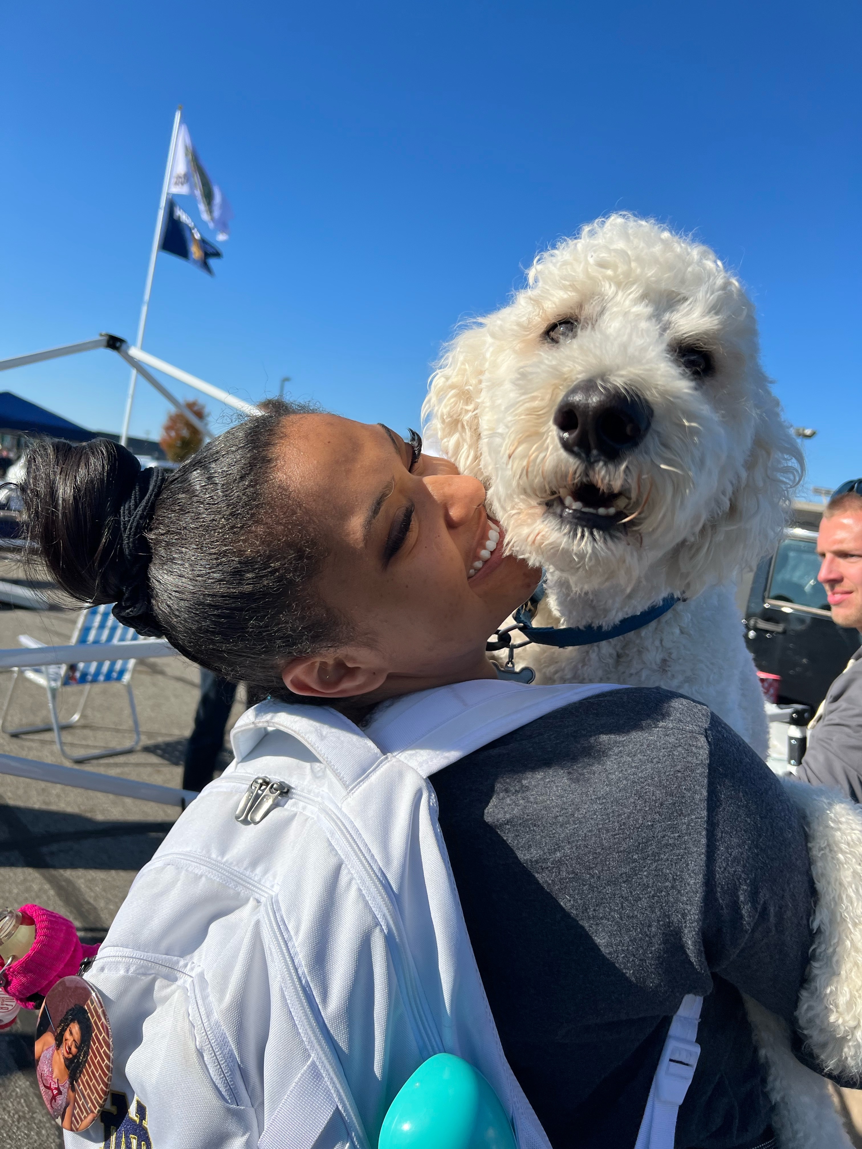 African American woman grinning widely while holding a white dog that appears to be smiling.