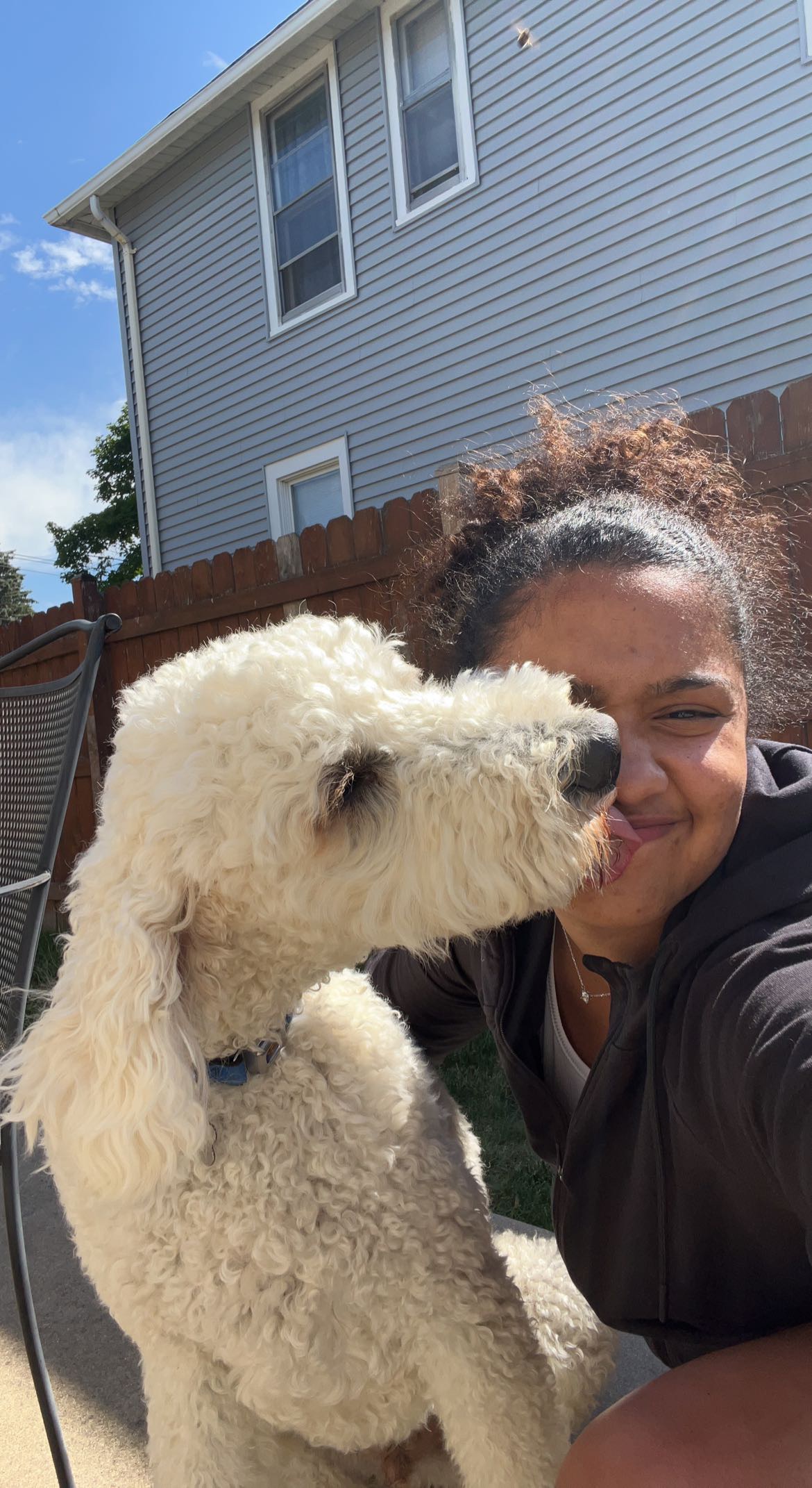 African American woman receiving a nose lick from a white dog.